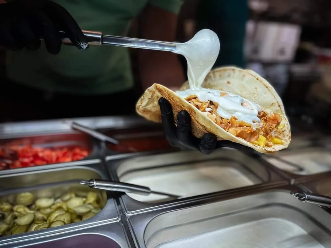 Mâna unui bucătar toarnă sos peste o shawarma deschisă